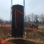 Un grand tuyau Weholite vertical suspendu au-dessus d’un trou dans un chantier de construction sur le point d’être descendu sous terre.