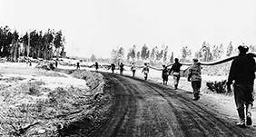 Scène historique en noir et blanc montrant les ouvriers originaux d'InfraPipe transportant un long tuyau à pied.