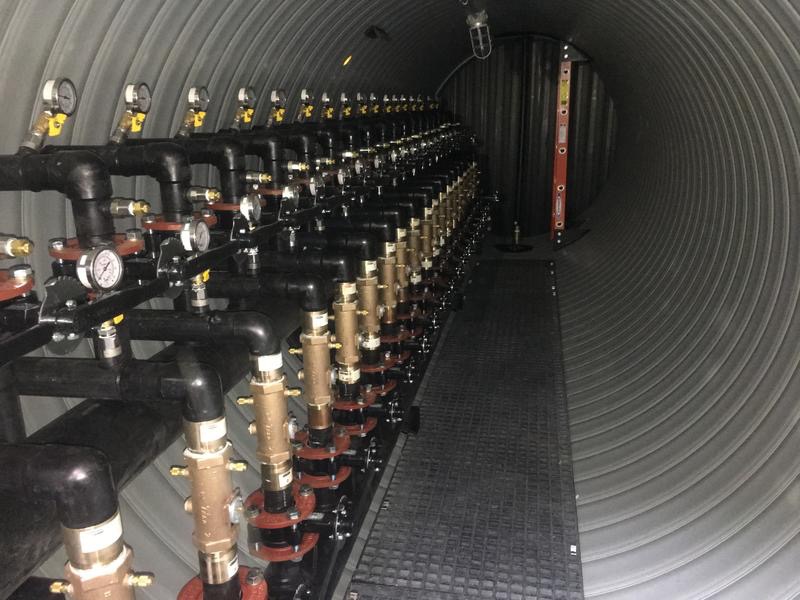 Inside of geothermal vault with a multitude of valves and gauges lining one side of the vault.