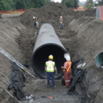 Construction workers installing underground pipe in a large dig site.