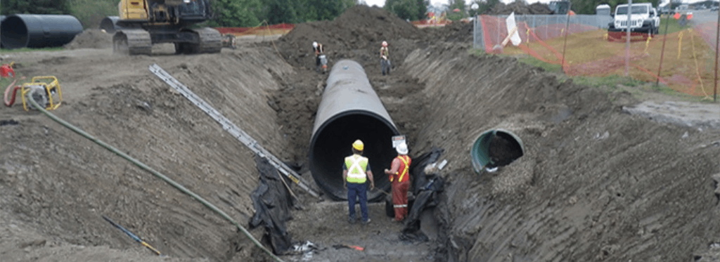 Construction workers installing underground pipe in a large dig site.