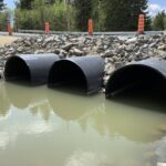 Three Weholite pipes installed under a road for water to pass through.