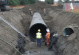 Construction workers installing underground pipe in a large dig site.